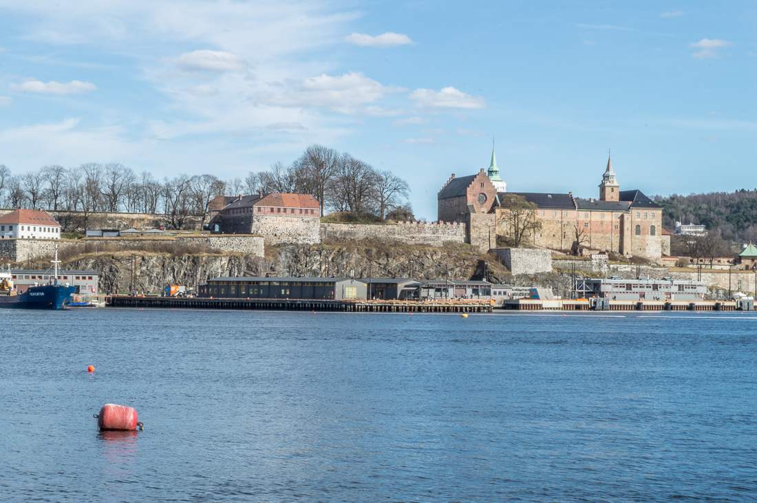 24 Hours in Oslo: This photo shows Akerhus Fortress in a distance, overlooking a large body of water on a sunny day.