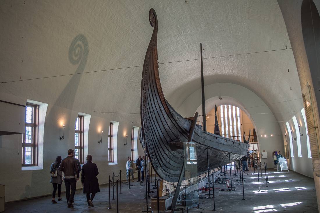 24 Hours in Oslo: This picture shows an old Viking ship on exhibition at the Viking Ship Museum in Oslo. It fills an entire hall. Some people are walking around it.
