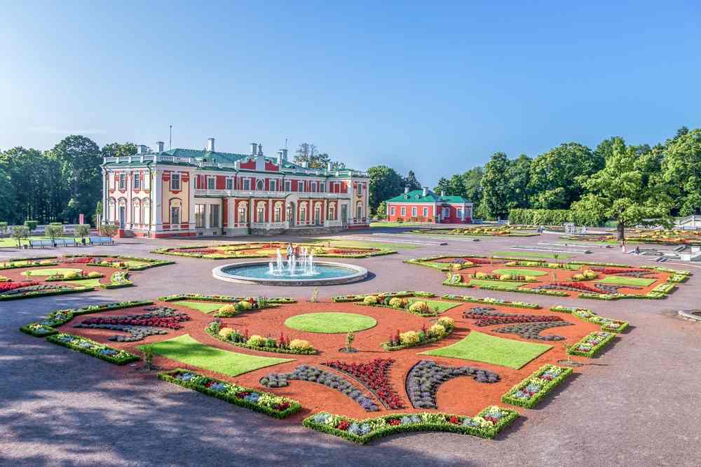 Tallinn sightseeing: The elegant exterior of the Kadriorg Palace features an Italian Baroque design with light red walls and a green roof. A well-manicured garden lies in front of the palace. 