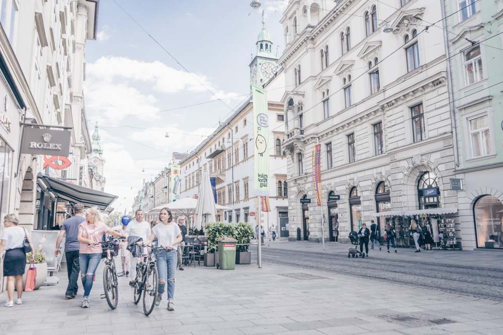 Young people with bikes walking down the main shopping street in Graz.