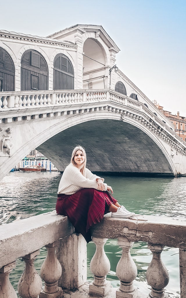 Beautiful woman sitting on a ledge with the famous Rialto Bridge in the background.