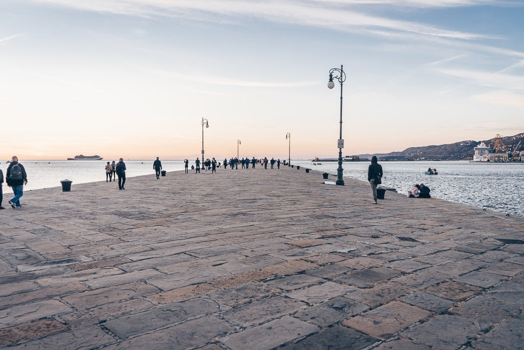 People taking a stroll on the Audace Pier (Molo Audace) in Trieste at sunset.