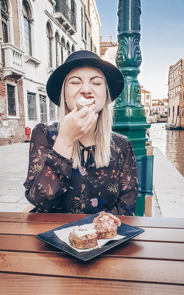 Gorgeous woman seated at a table taking a bite of tasty Venice cicchetti 