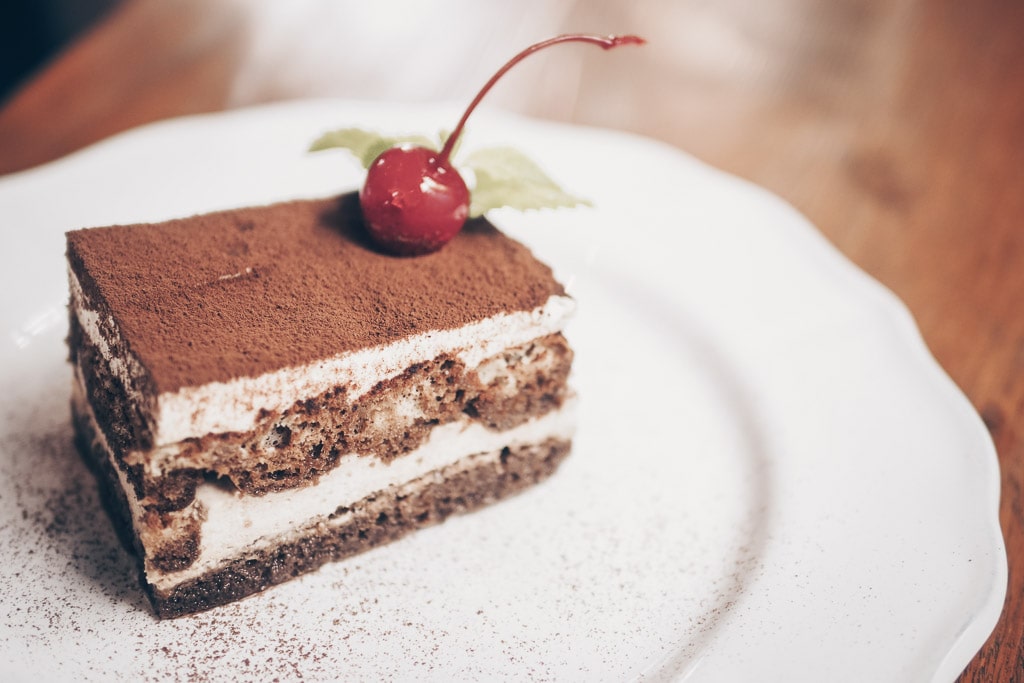 Venice Food: A slice of classic Italian tiramisù on a plate topped with a cherry.