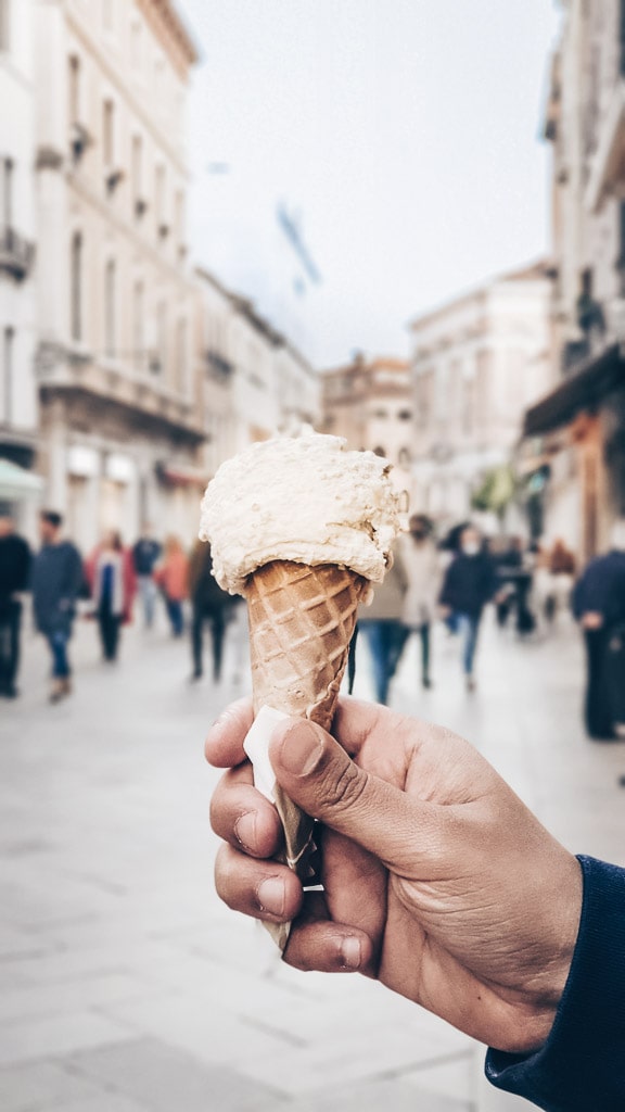 Man holding a cone of pistachio gelato (Italian ice cream) on a street in Venice.