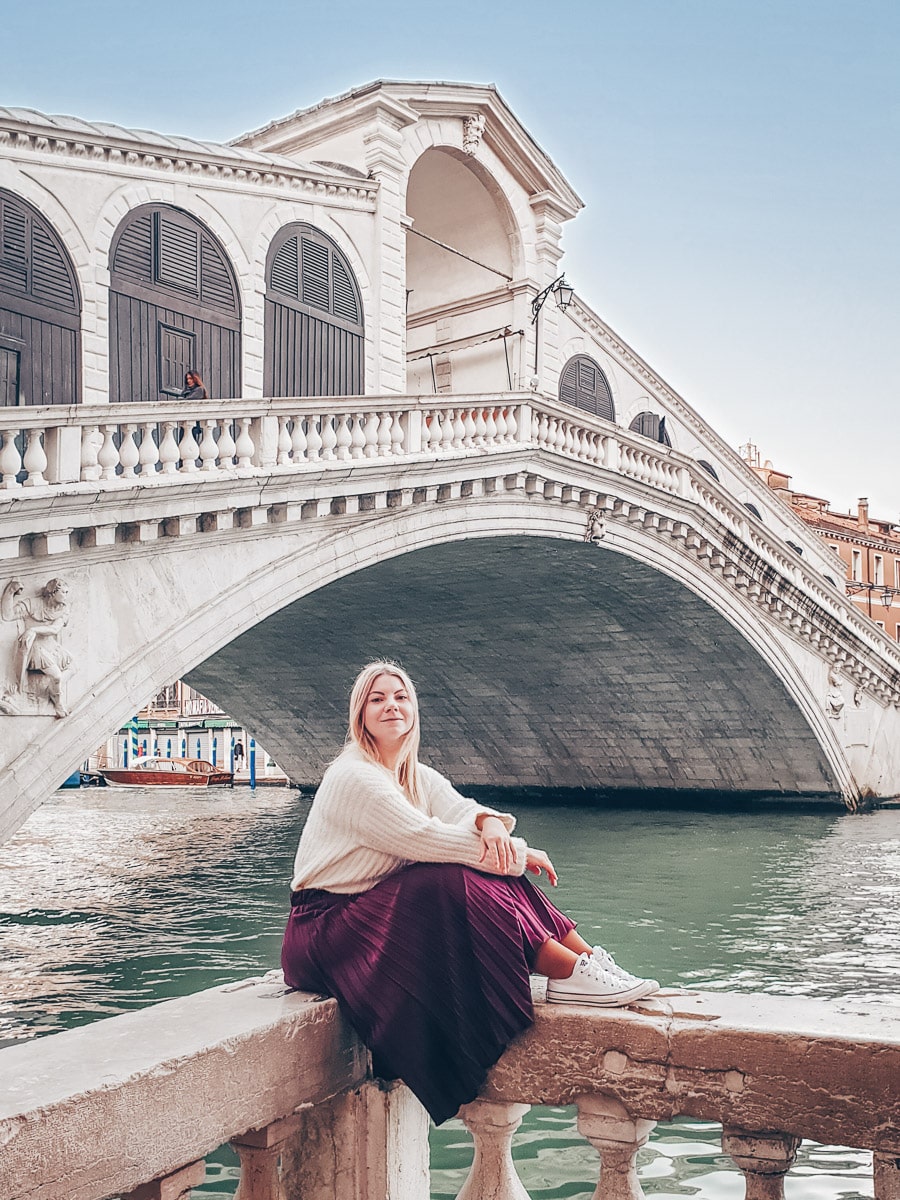 Best Venice Instagram Photo Locations: Woman sitting on a ledge in front of the Rialto Bridge