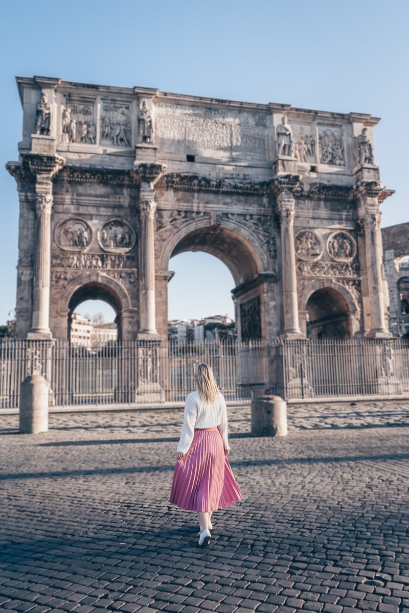 Rome historic sites: A woman posing for a photo in front of the imposing Arch of Constantine in the early morning